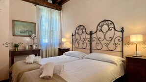 Une chambre d’hôtel avec deux lits, une tête de lit en bois, une table de chevet avec une lampe, une petite table sur laquelle est posé un vase de fleurs, et un tableau au mur.