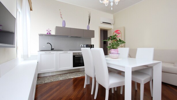 A modern kitchen with white cabinets, a built-in oven, and a microwave. There is a dining table with white chairs and a chandelier above. - Apt. Splendid Venice (250m from St. Mark´s Square) (Venecia)