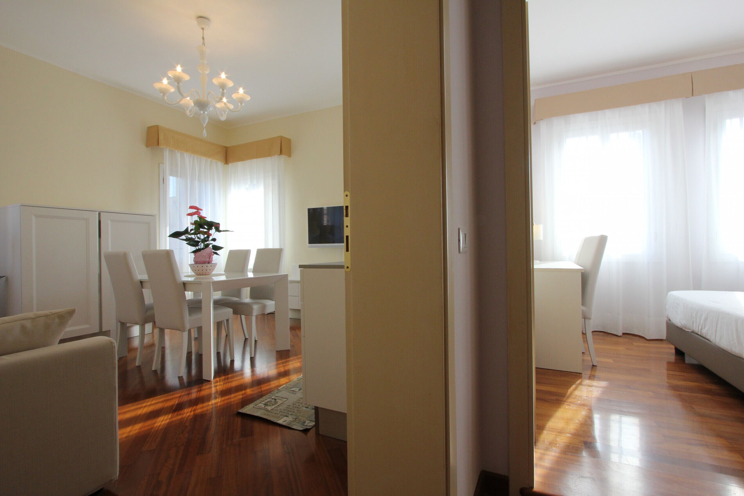 Habitación de hotel con piso de madera, zona de comedor con mesa y sillas, cama y televisor en la pared.