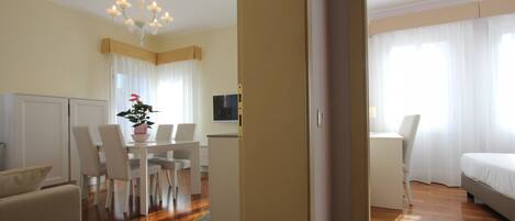 Habitación de hotel con piso de madera, zona de comedor con mesa y sillas, cama y televisor en la pared.