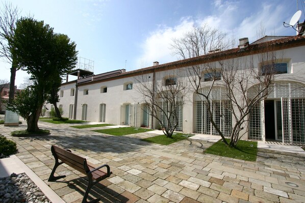 A courtyard with a bench, a building with multiple windows and a satellite dish, and a tree. - Apartment Baia (Historical Center) (Venecia)