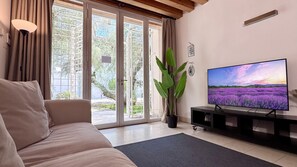 A living room with a sofa, a television, a potted plant, and a sliding glass door leading to an outdoor area.