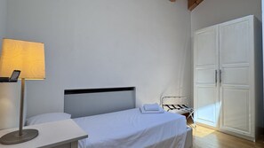 Una cama individual con ropa de cama blanca, una mesita de noche con lámpara y un armario de dos puertas.