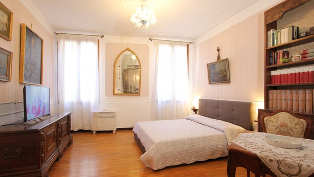 A room with a bed, a wooden dresser, a table with a lace tablecloth, a bookshelf, and a chandelier. - Corner Canal View (300m from Rialto´s Bridge) (Venecia)