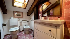 A bathroom with a toilet, bidet, and sink, wooden beams on the ceiling, and a tiled floor. - Zaffiro Grand Canal View (Venecia)
