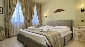 Quarto de hotel bem arrumado, com uma cama grande, uma mesinha de cabeceira, um criado-mudo e uma luminária fixada na parede.