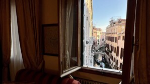 Quarto com janela dando para um canal estreito em uma cidade histórica.