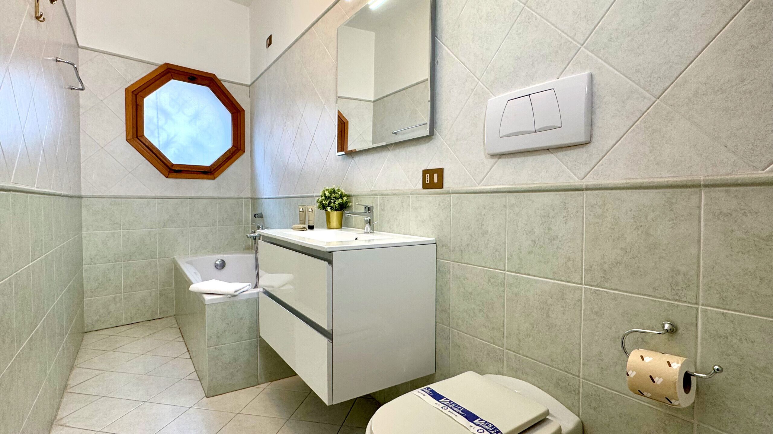 A bathroom with a toilet, sink, and bathtub. There is a window with a wooden frame, a mirror, and a towel rack.