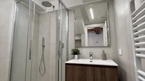 Une salle de bain moderne avec une douche à parois de verre, un meuble-lavabo en bois, un grand miroir et un porte-serviettes.