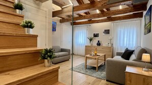 En moderne stue med trappe, træbjælker, sofa, sofabord og fjernsyn.