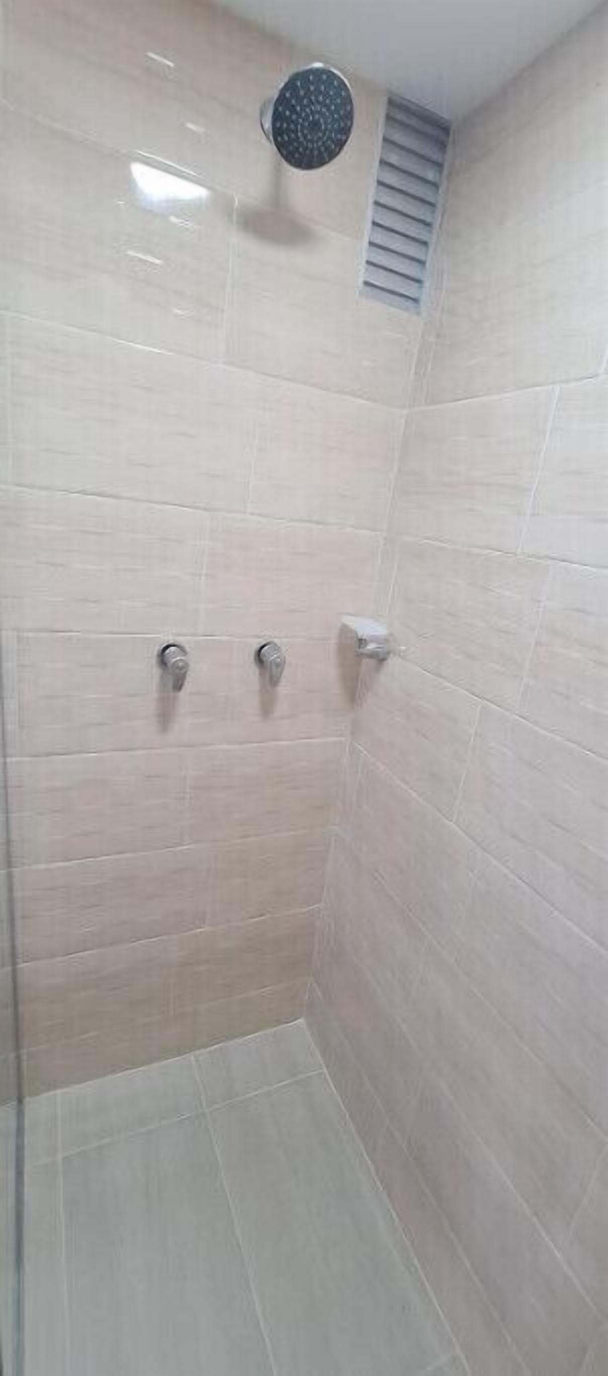 Une petite salle de douche carrelée, dotée d’un drain rond et d’une grille d’aération.