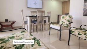 A hotel room with a dining table, chairs, a bed with a tropical print, and a TV mounted on the wall. - 207 AKUA RESORT® VACATION APARTMENT (Ricaurte)