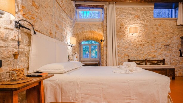 A stone-walled room with a bed, a wooden nightstand, a bench, and a window with a view of greenery. - Macchiaroli La Gioiosa Castle the magic of a medieval castle in Teggiano (Teggiano)