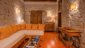 A cozy room with a stone wall, wooden ceiling beams, a sofa with orange cushions, a coffee table with books, and a wooden cabinet. - Macchiaroli La Gioiosa Castle the magic of a medieval castle in Teggiano (Teggiano)