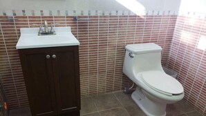 A bathroom with a toilet, a cabinet, and a tiled backsplash. - Gran Hotel Alijadores (Tampico)