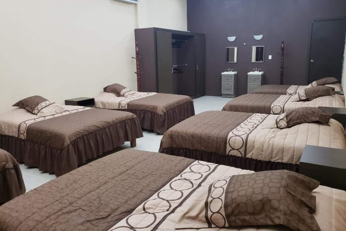 A hotel room with four beds, a wardrobe, a vanity with two sinks, and a mirror.