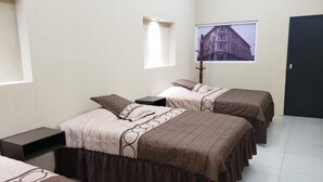 A hotel room with two beds, a nightstand, a lamp, a window with a view of a building, and a door. - Gran Hotel Alijadores (Tampico)