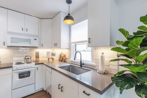 A modern kitchen with white cabinetry, a stainless steel sink, a kettle, and a potted plant.