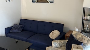 Un saló modern amb un sofà blau fosc, una butaca estampada, una taula de centre i un quadre d'un moll.