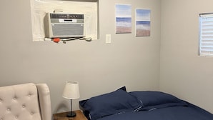 Un dormitori amb un llit, una cadira, una tauleta de nit, una làmpada i dos quadres al mur.