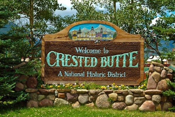 A welcome sign for Crested Butte National Historic District with a rustic stone border and a painted town scene.