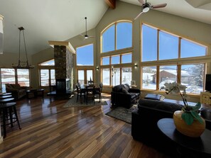 A spacious living room with a fireplace, large windows, and a stone wall.