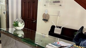 Een receptiebalie van een hotel met een glazen blad, een houten deur en een bordje voor 'Botanic Garden Hostel'.