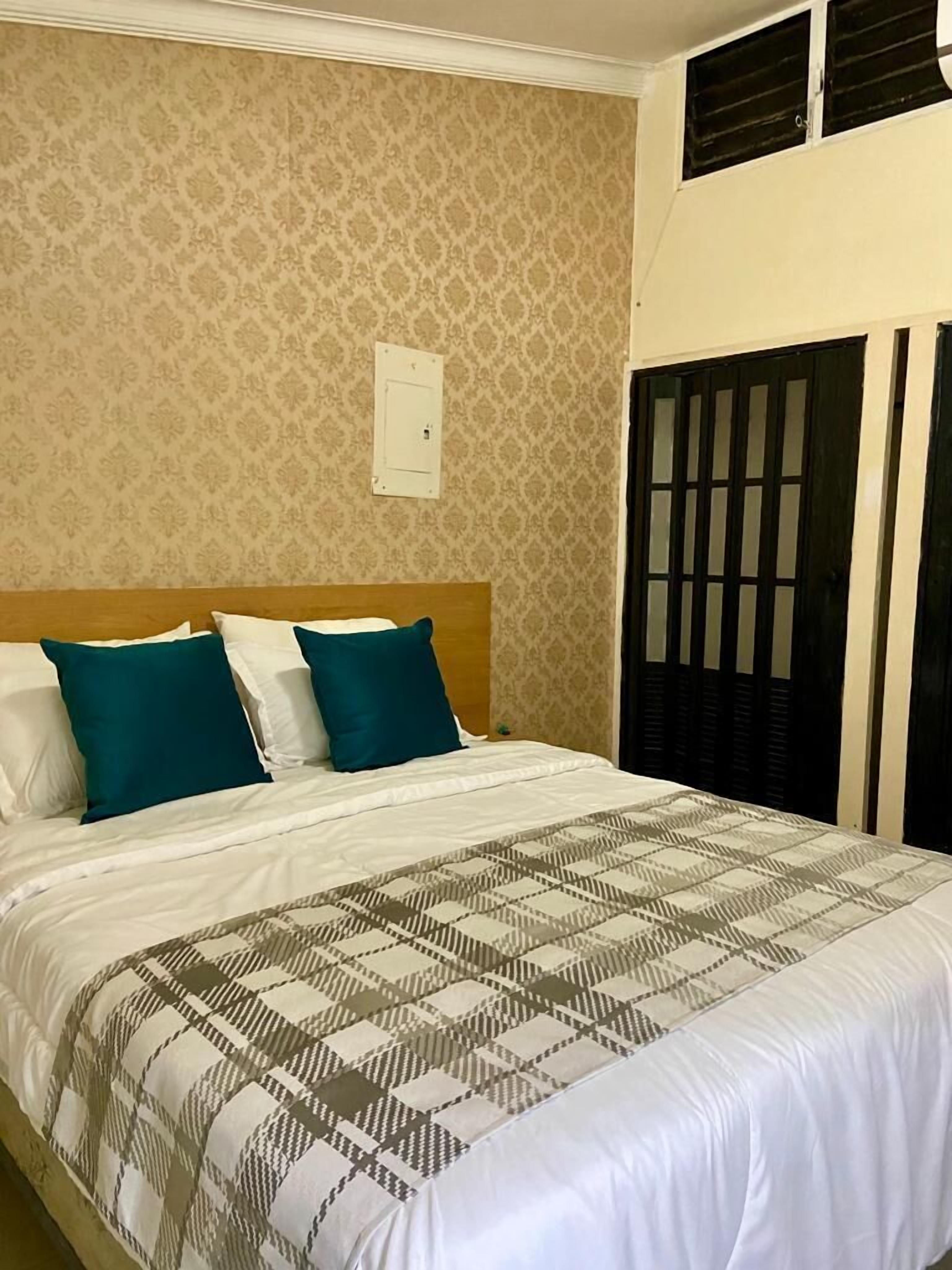A hotel room with a bed, a patterned wall, a window with blinds, and a door with a window.