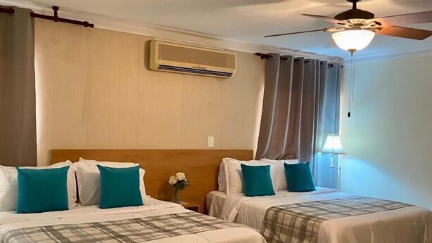 Een hotelkamer met twee bedden, een plafondventilator, een airconditioning en een nachtkastje met een lamp.