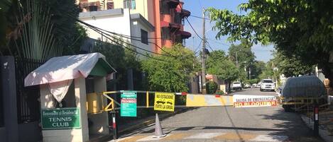 A gated residential area with a tennis club sign, a no parking sign, and a barricade indicating an emergency exit.