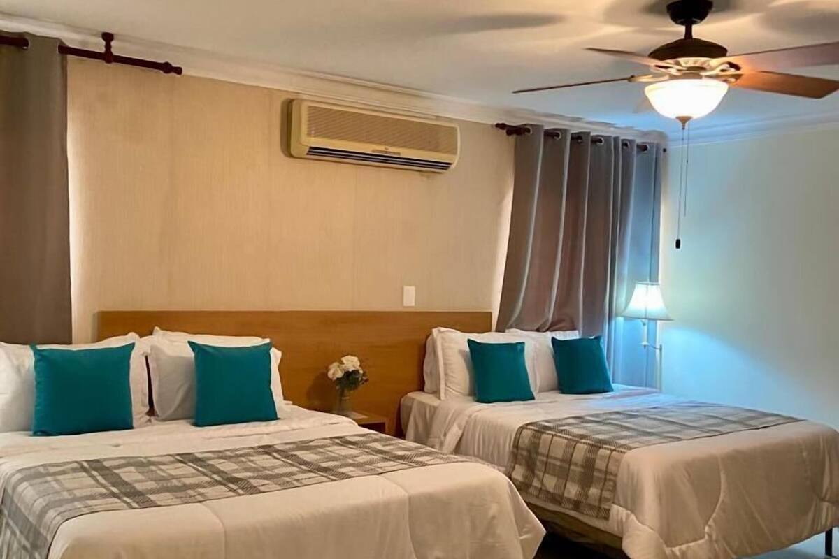 Een hotelkamer met twee bedden, een airconditioner, een plafondventilator en een nachtkastje met een lamp.