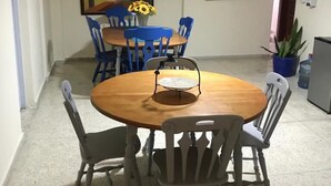 Een eetgedeelte met een ronde houten tafel, blauw-witte stoelen, een plafondventilator en een schilderij aan de muur.