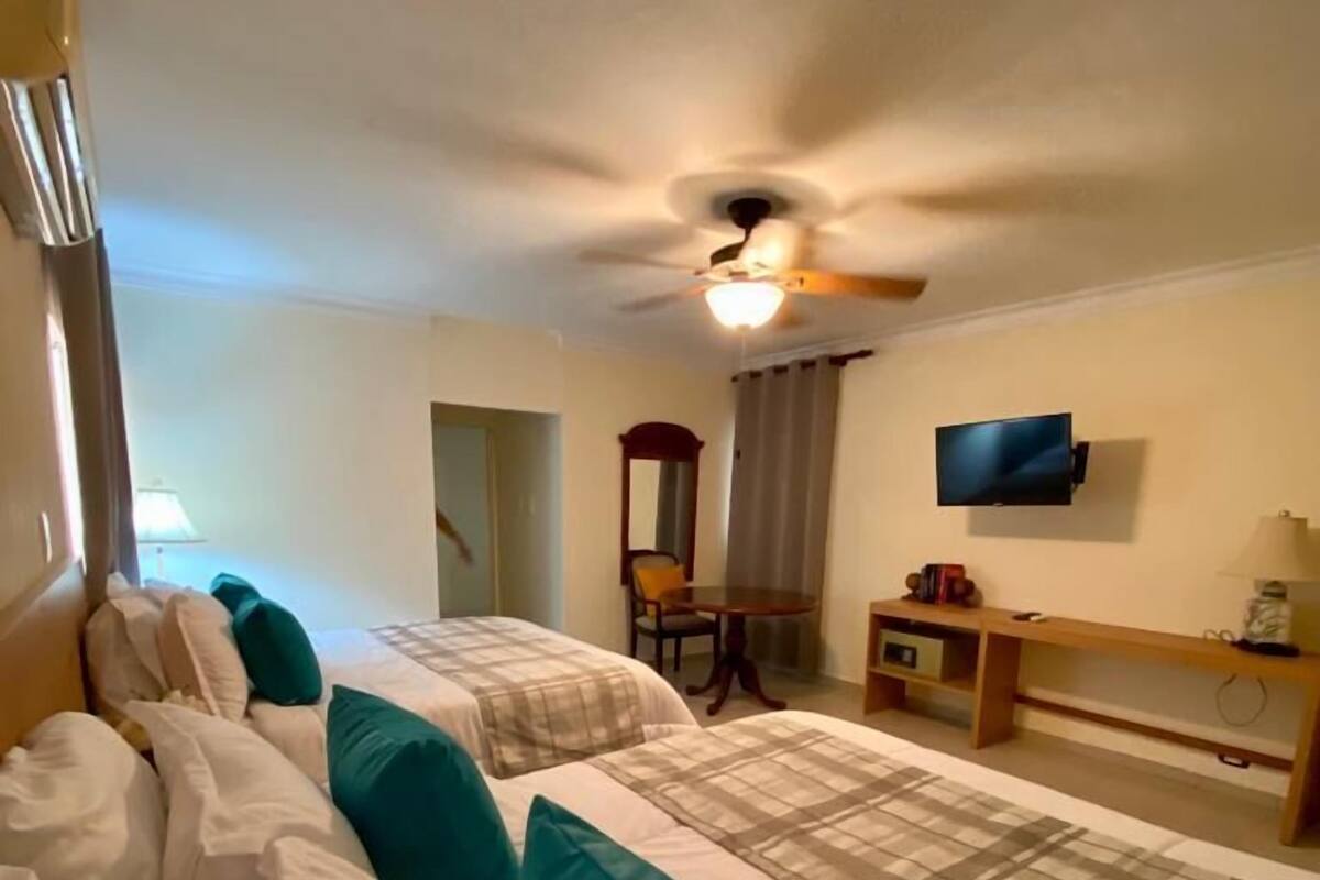 Een hotelkamer met twee bedden, een bureau, een stoel, een televisie en een plafondventilator.