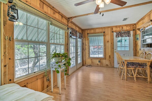 A wooden cabin interior with large windows, a dining table, and chairs.