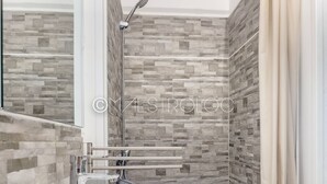 Een moderne badkamer met een achterwand van stenen tegels, een witte wastafel en een douche met een handdouche.