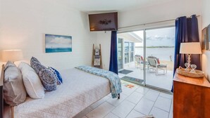 Ein Schlafzimmer mit Bett, Fernseher, Gemälde und Blick ins Freie.