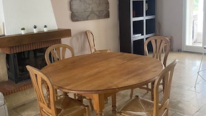 Een eetruimte met een houten tafel en stoelen, een open haard, een wereldkaart kunstwerk en een boekenkast.