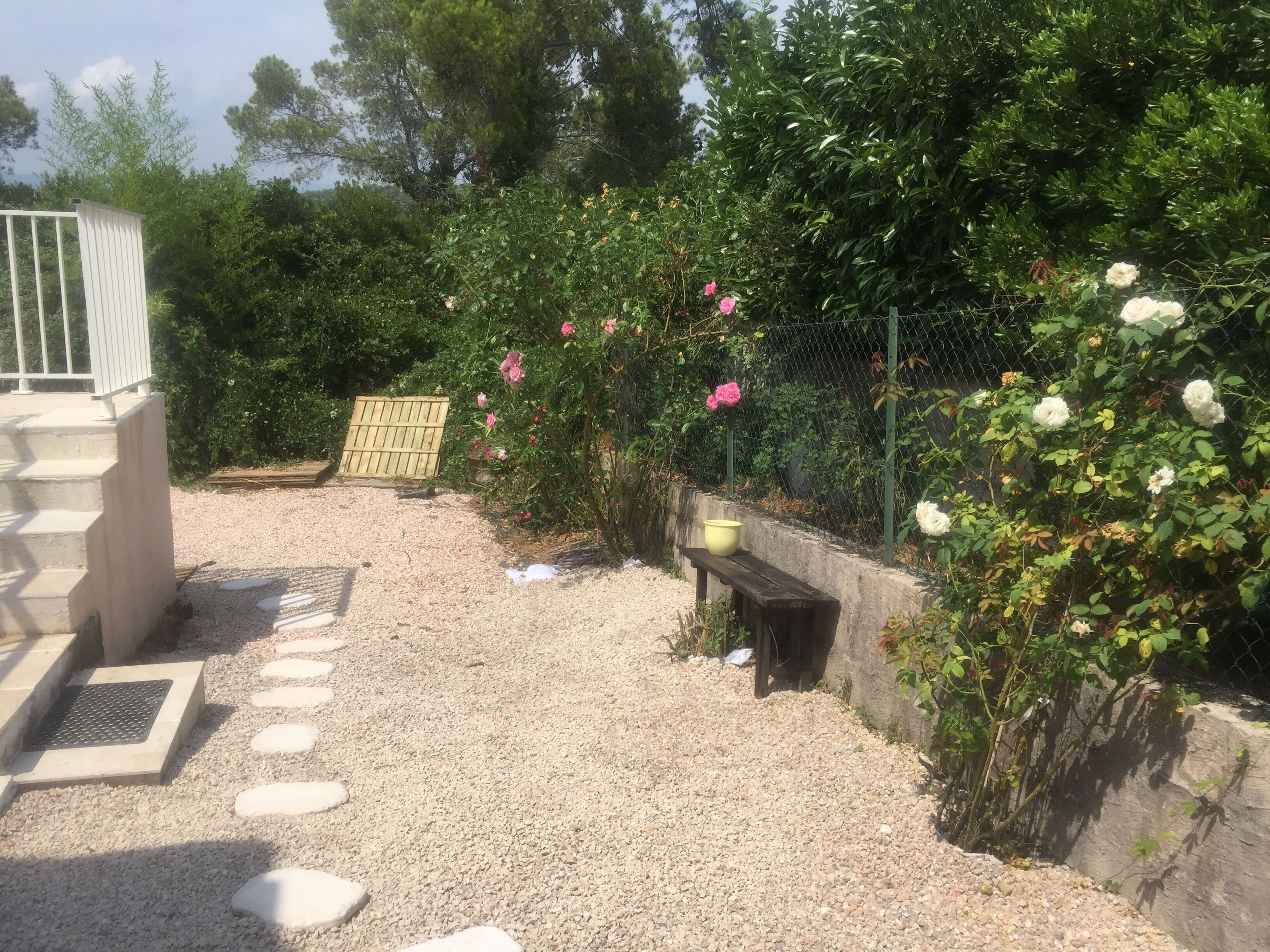 Un giardino con sentiero in pietra, una panchina di legno e un cancello in metallo.