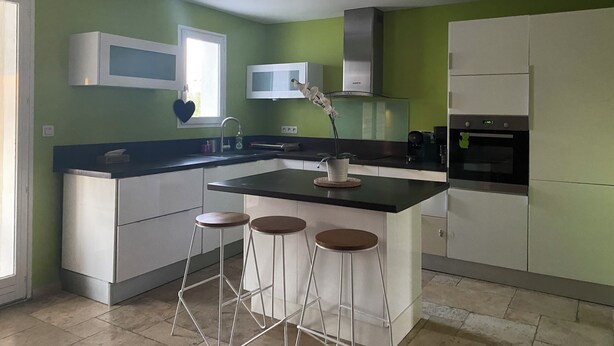 Een moderne keuken met een centraal kookeiland, barstoelen, een magnetron en een koelkast.