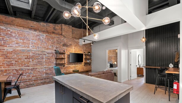 Een moderne keuken met een centraal eiland, open bakstenen muren en een hanglamp.