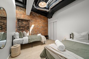 A modern bedroom with a brick wall, two beds, a mirror, and a small bedside table. - The Goodman: Front Street Flats (Belleville)