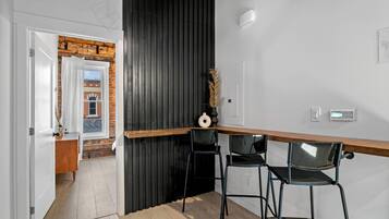 A modern kitchen with a wooden countertop, black bar stools, and a view of a brick building through an open door.