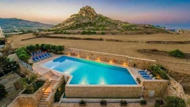 A swimming pool with a view of a hill and distant landscape. - Red Rose.. (Iz-Zebbug)