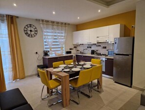 Eine moderne Küche mit weißen Schränken, einem Edelstahlkühlschrank und einem Essbereich mit gelben Stühlen und einem Holztisch.
