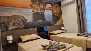 A hotel room with a large rock formation painting on the wall, two beds with beige bedding, and a window with curtains. - Red Rose.. (Iz-Zebbug)