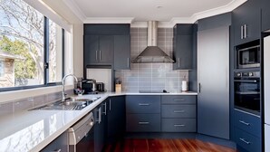 Une cuisine moderne avec des meubles de couleur sombre, une hotte de cuisine en acier inoxydable et un four encastré.