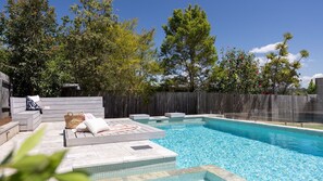 Relax by the serene pool surrounded by lush greenery and trees, with a comfortable seating area nearby.