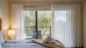 Relax in a serene space with a large bed, bedside lamp, and sliding glass door leading to a peaceful outdoor area.