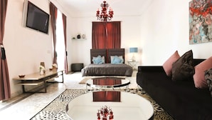 A modern hotel room with a bed, a black sofa, a round coffee table, a TV, and a chandelier. - Riad VIP (Marrakech)