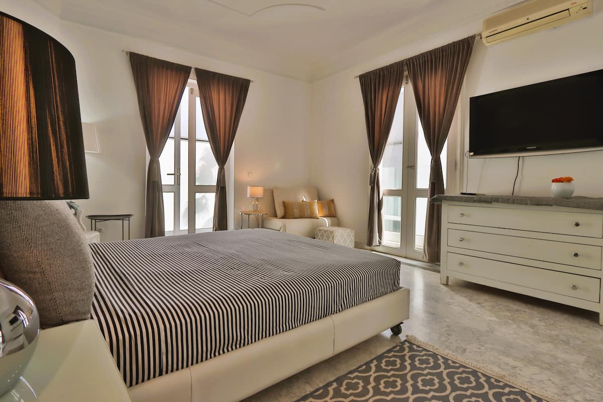 A bedroom with a large bed, a dresser, a TV, and a window with curtains.